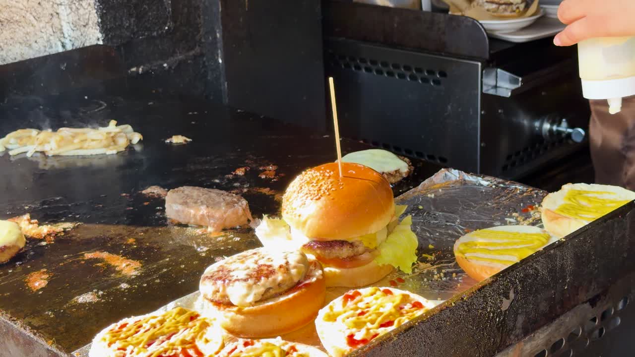 シェフが鉄板でパティを焼きながら、ごまバンズにマスタードとソースを絞りかける。