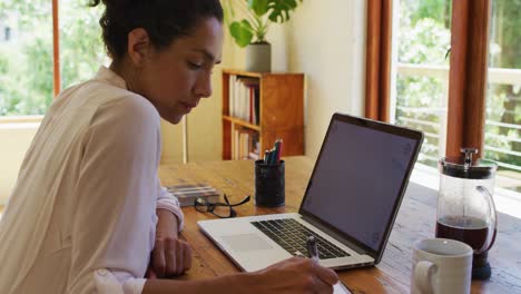 Caucasian-woman-using-laptop-and-writing,-working-from-home