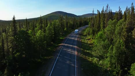 drone shot over a camper van on a arctic forest road, driving toward fells, summer evening