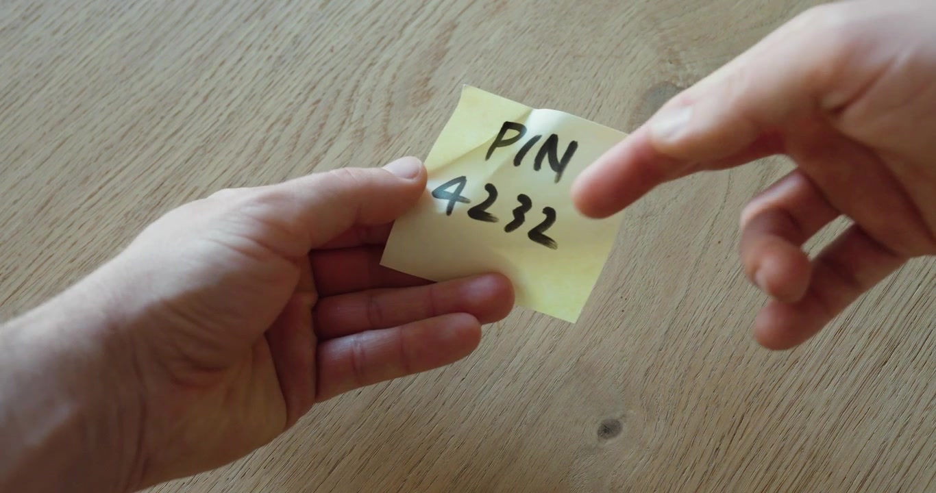 Close-up of a handwritten PIN code on a paper note being passed from hand to hand, symbolizing unsafe data sharing, privacy risk, and poor security behavior.