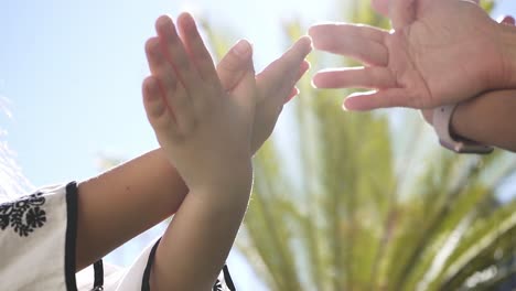 Mother-and-daughter-playing-together-while-making-a-bird-with-his-hands-in-the-air-in-slow-motion,-in-a-bright-and-sunny-day,-with-a-palm-in-the-background