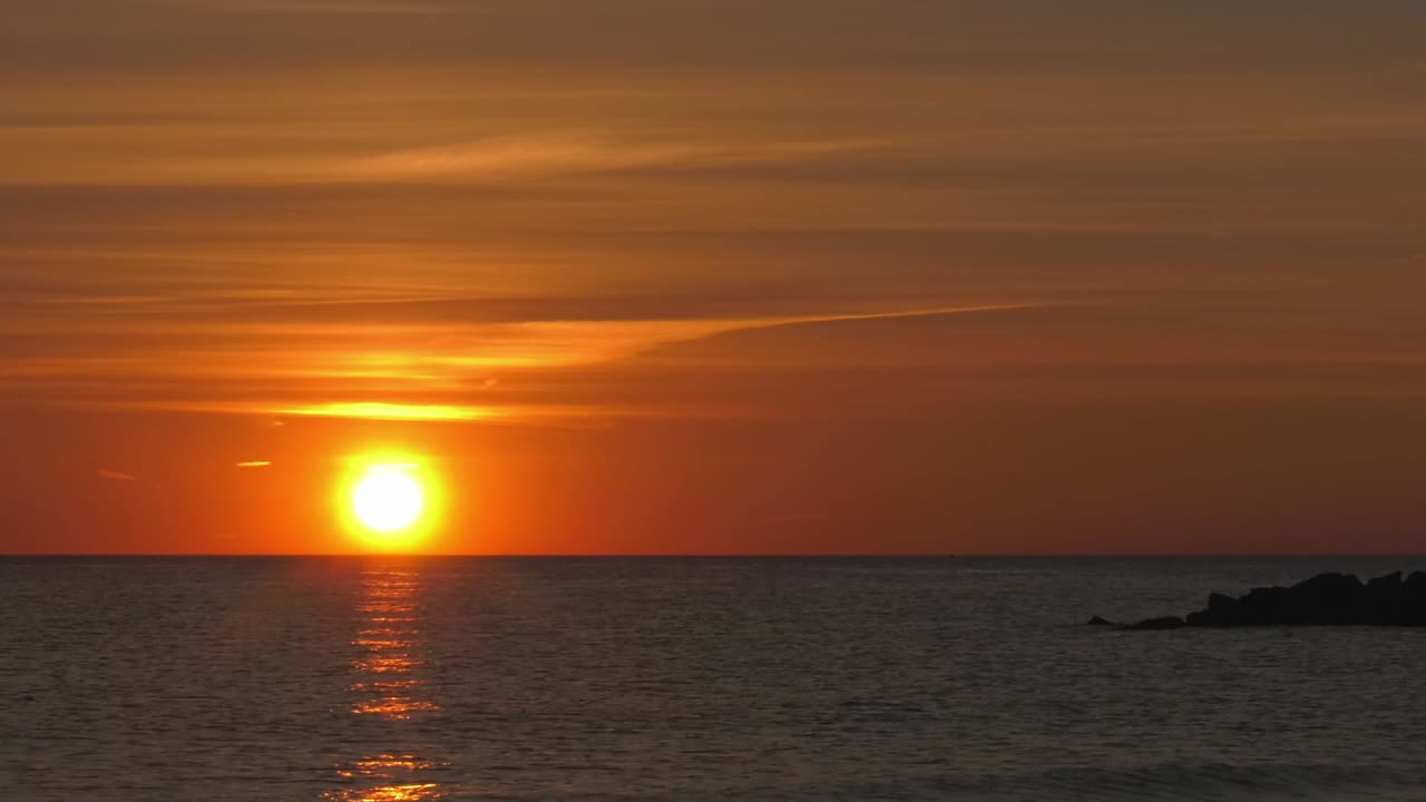 Dramatic sunrise timelapse, sun rising over ocean horizon into orange skies with clouds moving
