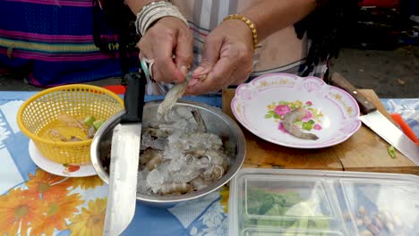 old hands peeling and preparing shrimp at open air kitchen, additional vegetables on table - medium direct shot