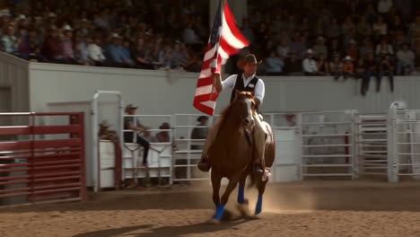 cowboy carrying american flag on horseback at a rodeo event