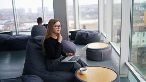 female freelancer working on a laptop. beautiful business woman sitting in a comfortable soft chair and typing on a wireless computer. panoramic window view.