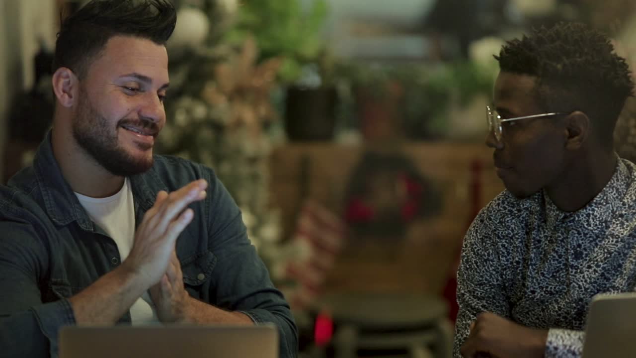 hombres felices hablando mientras trabajan con computadoras portátiles en un café