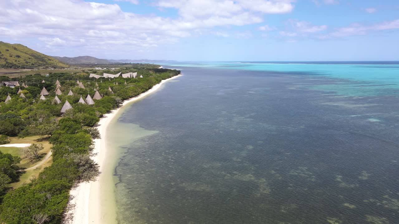 Drone aerial moving forward over a blue beach in New Caledonia