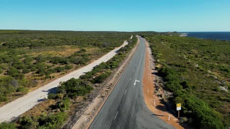 long tarmac road through shrubbery covered sandy terrain in western australia