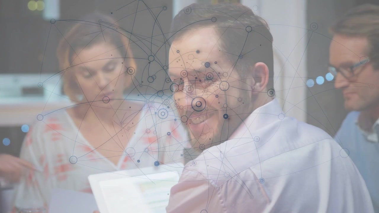 Team di quattro persone che esamina documenti in una riunione di lavoro, con un uomo che usa un tablet generando una sovrapposizione di dati per la revisione.