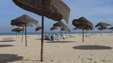 empty beach with woven parasols casting shadows on the sand by the mediterranean sea