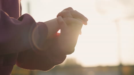 close-up of woman hand in maroon clothing making wrist twist with fingers locked together, sunlight creating a glowing effect around her hand in a peaceful outdoor setting