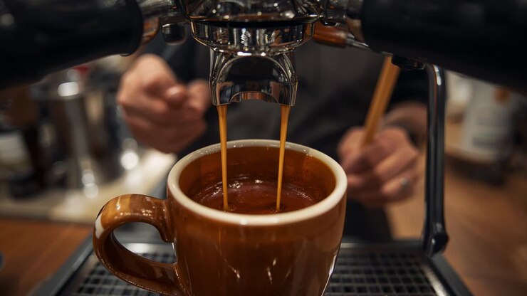 Barista con maniche scure che prepara l'espresso al bar, versando il caffè dalla macchina nella tazza