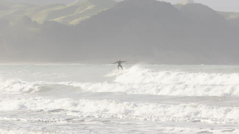 wide shot of a man catching waves on a sunny day in castle point, new zealand