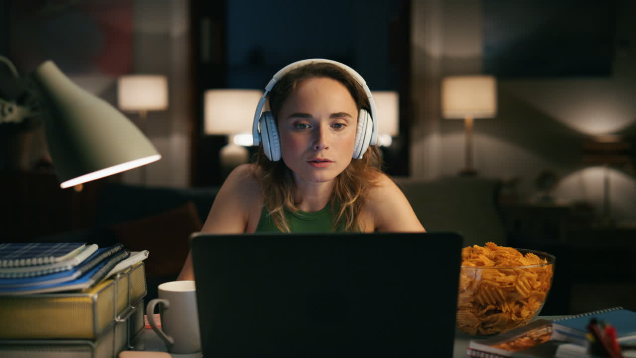 Involved freelancer working eating snacks at dark room. Calm girl watching movie