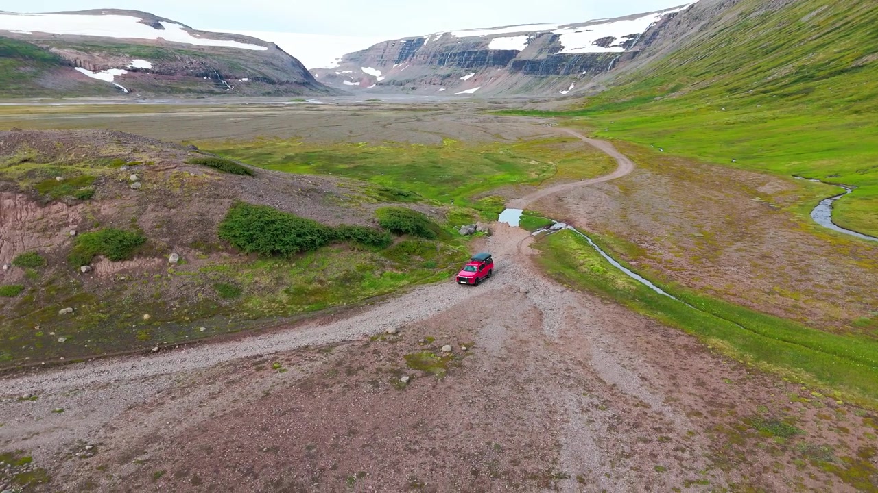 Inquadratura cinematografica dall'alto di un'auto 4x4 rossa che percorre una strada sterrata negli altopiani remoti dell'Islanda, vicino al ghiacciaio Drangajokull. Ideale per contenuti di viaggio, avventura e sostenibilità