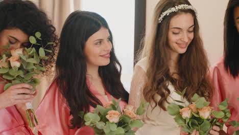 group of multiethnic female friends and bride wearing silk pink and white nighdresses and holding bouquets