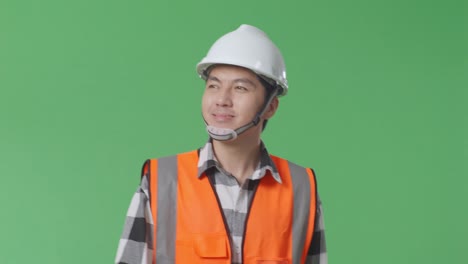 안전 헬을 입은 아시아 남성 엔지니어가 녹색 화면 배경 스튜디오에서 는 동안 손을 흔들고 있습니다.