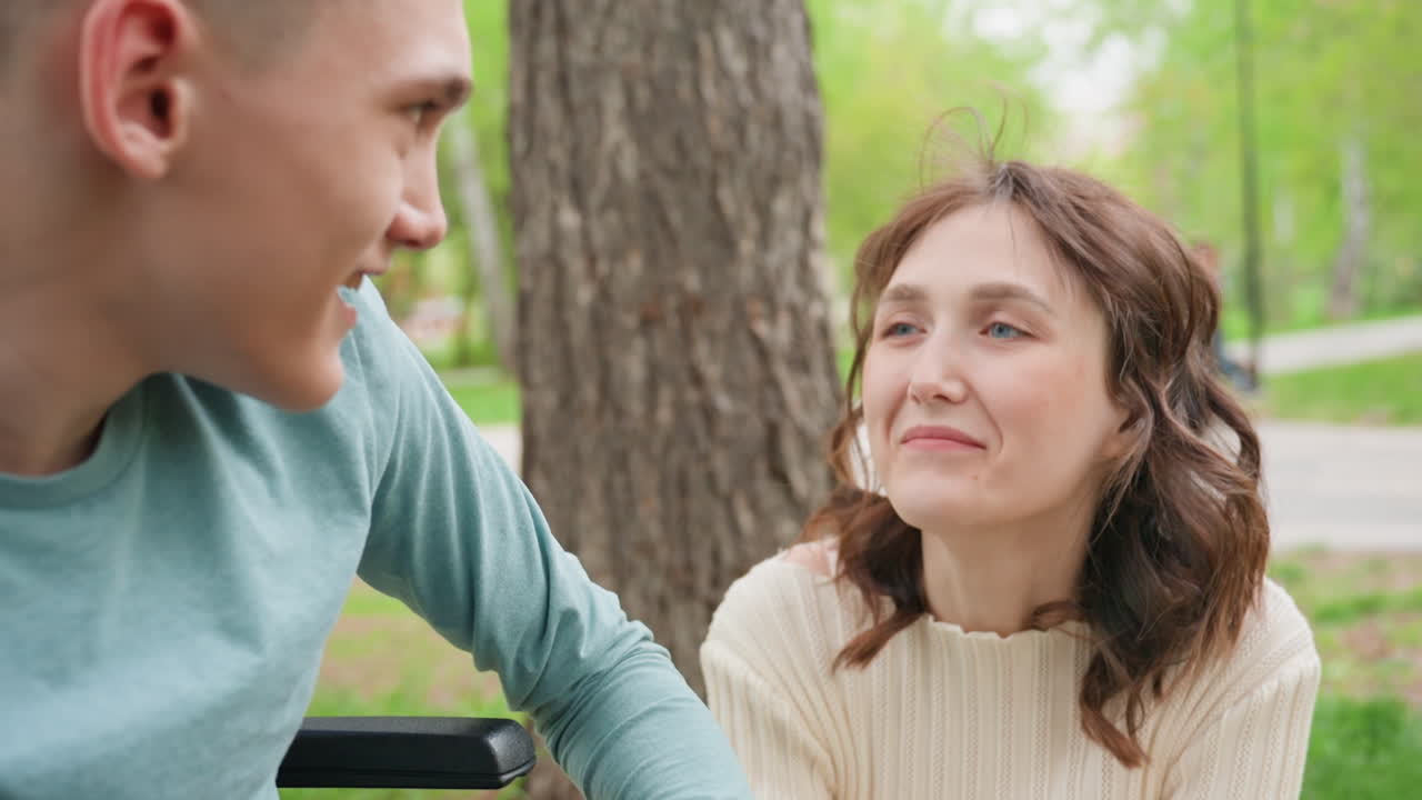 Gentle Talk Fosters Understanding Bond, Man In Youth Comforts Woman Amidst Blooming Trees And Calm Setting, Youthful Man Shares Heartfelt Moment With Older Woman On Park Bench During Springtime
