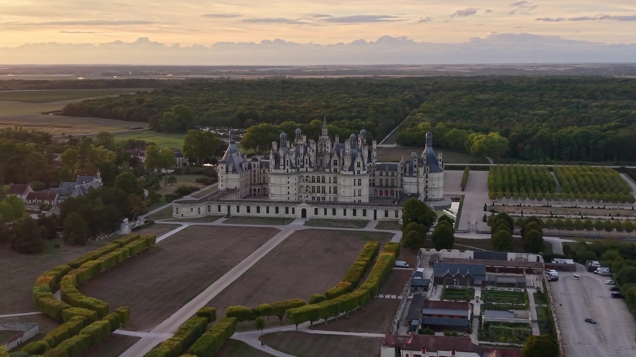 Riprese aeree cinematografiche mostrano il Castello di Chambord dall'alto, con la sua architettura rinascimentale ornata, i giardini geometrici, la foresta circostante e i terreni agricoli illuminati dalla luce serale
