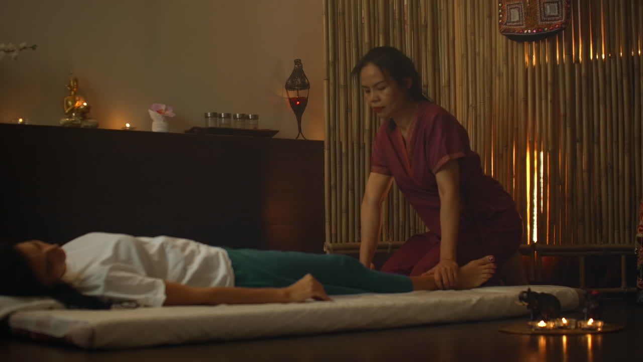 Medicina cinese alternativa: una donna asiatica esegue movimenti di massaggio terapeutico sulla schiena e sulle gambe di una donna caucasica sdraiata su un lettino. Massaggio tradizionale cinese