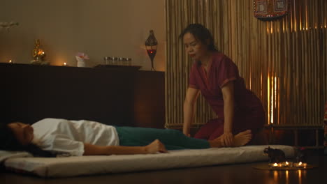 alternative chinese medicine an asian woman performs therapeutic massage movements on the back and legs of a caucasian woman lying on a couch. traditional chinese massage.