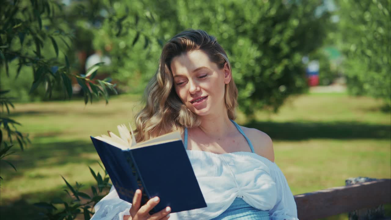 Giovane donna che legge un libro su una panchina in un parco soleggiato