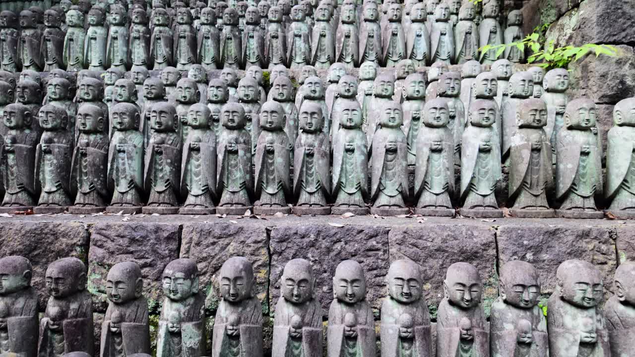 Slow camera movement from tight close-up to wide view of numerous moss-covered Jizo statues at a Japanese temple, with soft natural light and tranquil ambiance