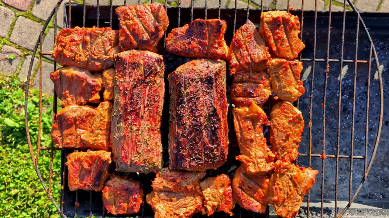 Large ribs and steaks sizzle on the grill, surrounded by smoky chops and kabobs