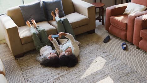 happy mixed race mother and daughter laying on the floor,having fun and taking selfie