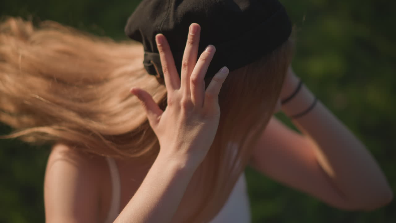 Ragazza dall’aspetto giovanile con le mani che incorniciano il viso, ragazza adolescente con cappello che crea forme giocose con le mani all'aperto, giovane ragazza che indossa un cappello nero ed esprime divertimento attraverso gesti con le mani in un parco soleggiato