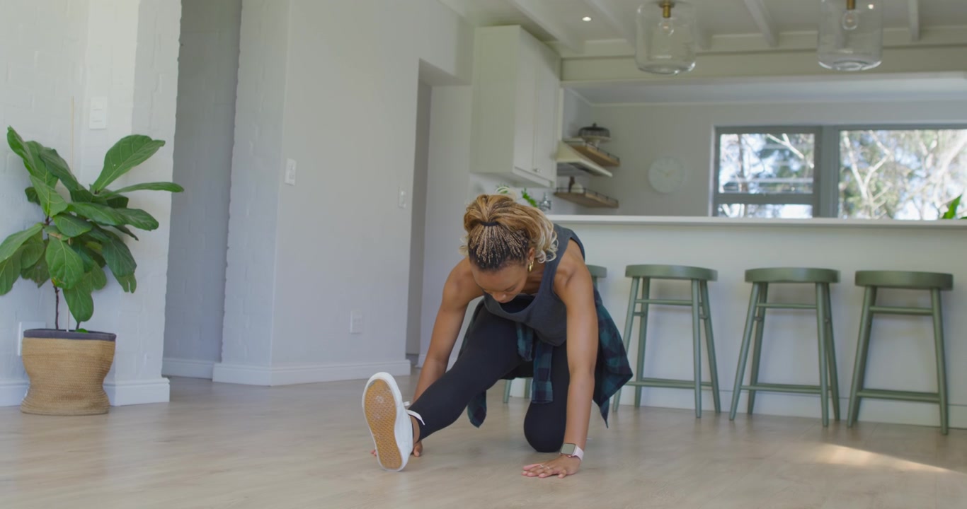 African American woman moving from deep lunge to hamstring fold in kitchen, deepening stretch