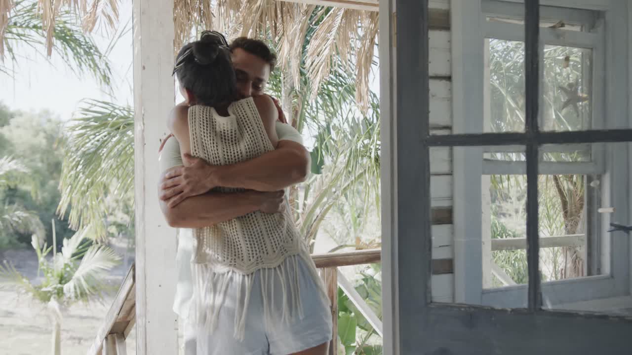 Coppia felice di etnie diverse che si abbraccia sul portico di una casa al mare assolata, al rallentatore.