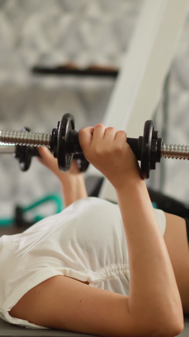 여성은 집에서 덤벨로 팔을 들어 올립니다. 집중된 젊은 운동선수 여성은 집에 기반의 피트니스 영역에서 무게로 팔 근육을 운동합니다.