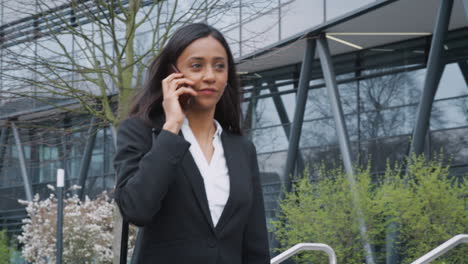 Mujer-De-Negocios-Viajando-Al-Trabajo-Hablando-Por-Teléfono-Móvil-Fuera-Del-Moderno-Edificio-De-Oficinas