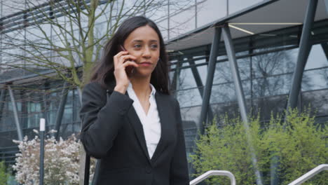 businesswoman commuting to work talking on mobile phone outside modern office building