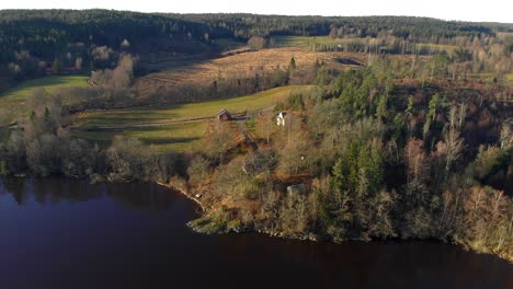 Vista-Aérea-De-Una-Casa-Pintoresca-En-Un-Campo-Colorido-Cerca-De-Un-Lago-En-Otoño