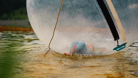 little girl pushes legs lying inside water ball in pond