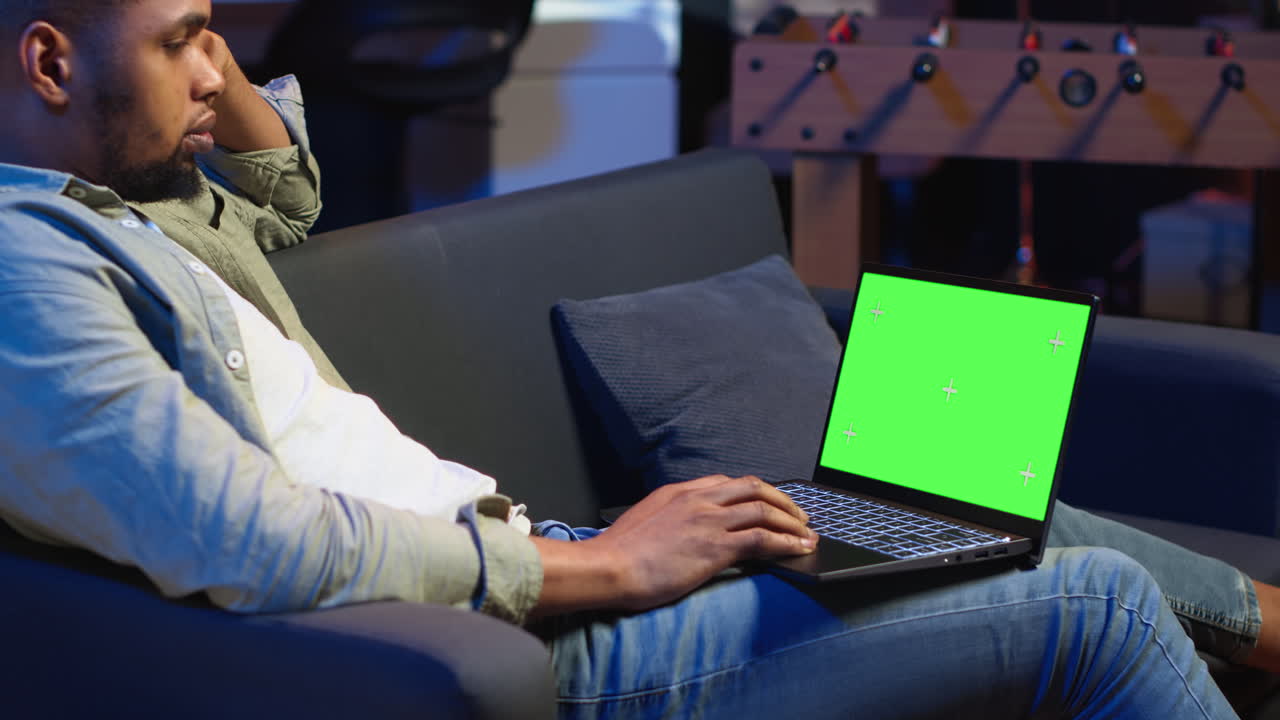 Vertical Video African american young guy using device with green screen from his sofa