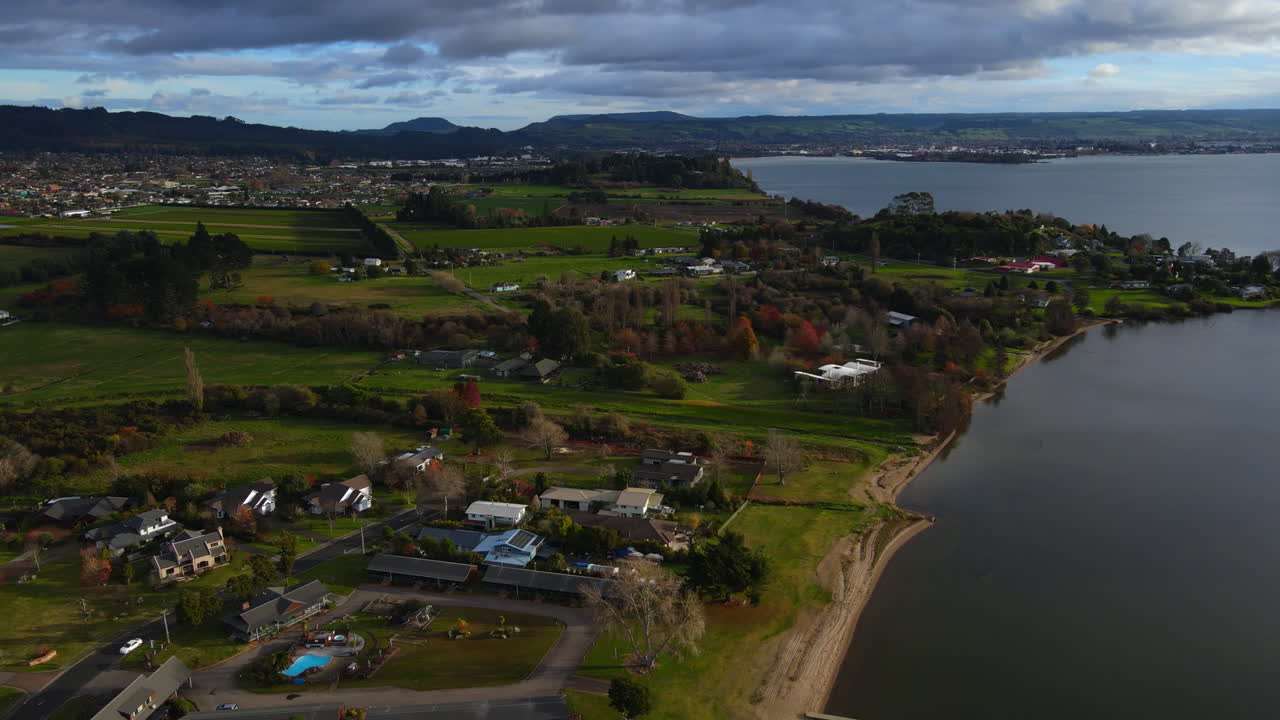 toma aérea de las casas de los suburbios de nueva zelanda junto a un lago, campos verdes y montañas