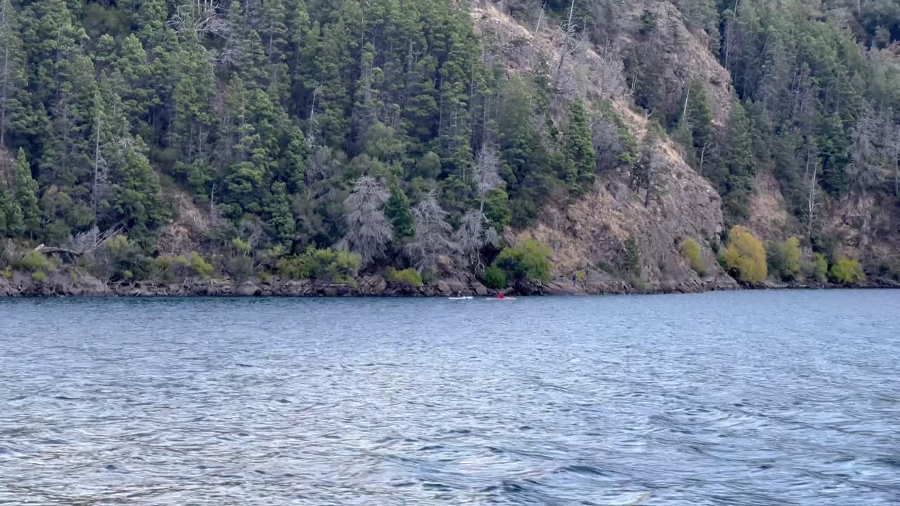 A calm scene by a forested lake in Patagonia, with a kayak visible on the water