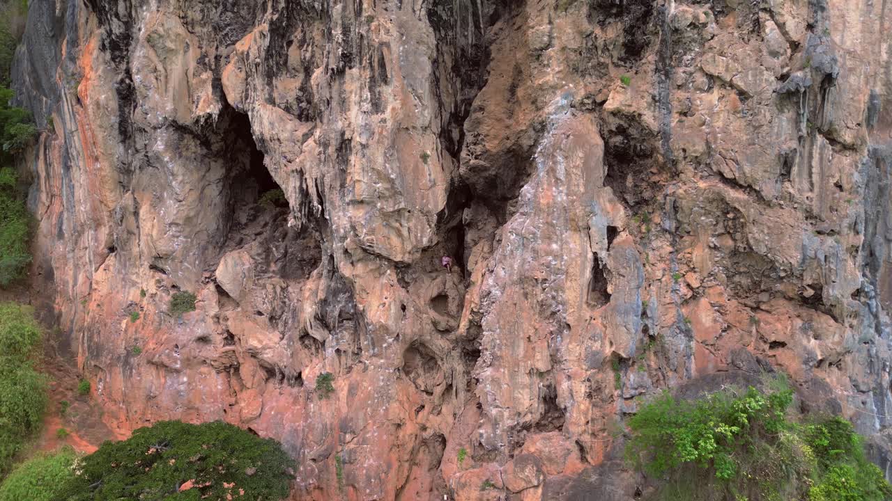 Rock climber resting during a difficult climb on Rai Leh beach cliff in Thailand. Gorgeous aerial view flight fly reverse drone