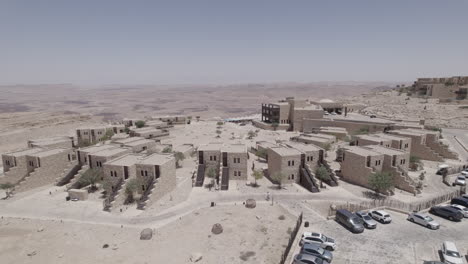 Aerial-view-over-a-beautiful-architecture-stone-built-hotel-on-a-crater-cliff-desert-landscape,-crossing-the-accommodations-and-over-the-pool