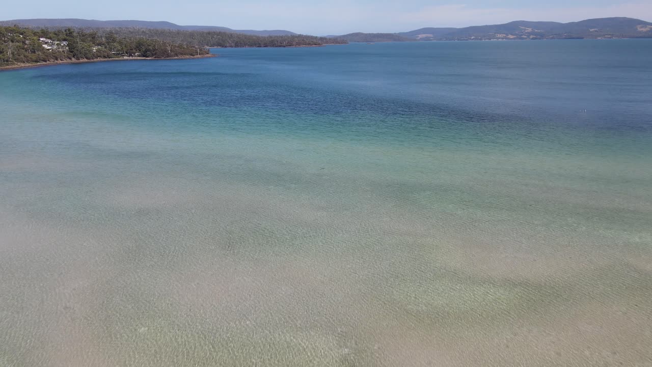 la antena del dron avanza sobre el agua azul tropical en la playa de arena de tasmania