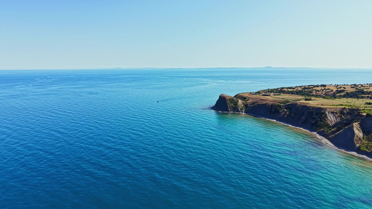Vista della costa a mezzogiorno che mostra acqua limpida e terra in lontananza con una piccola barca in mare.