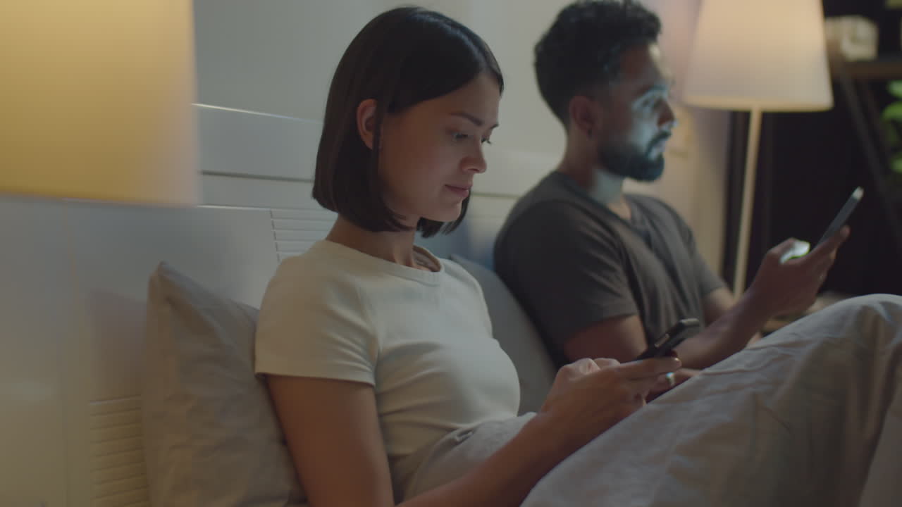 밤에 침대에서 드폰을 사용하는 부부