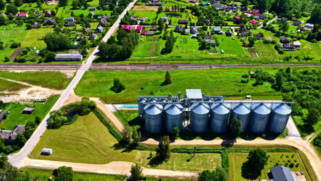 grain silos in green landscape near village surrounded by fields and houses in drone video