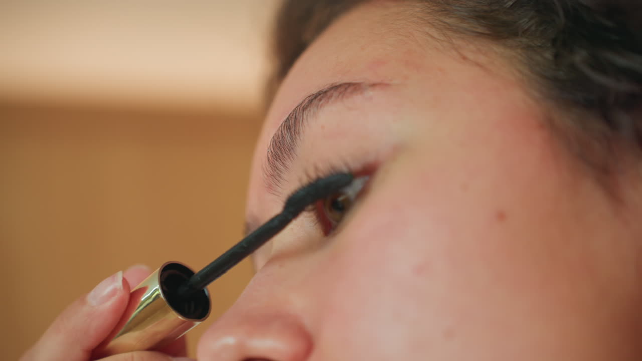 Closeup shot of eye with mascara application. Focused view of eye with precise mascara brush strokes. Intimate scene of eye being carefully beautified with makeup in cozy hotel setting