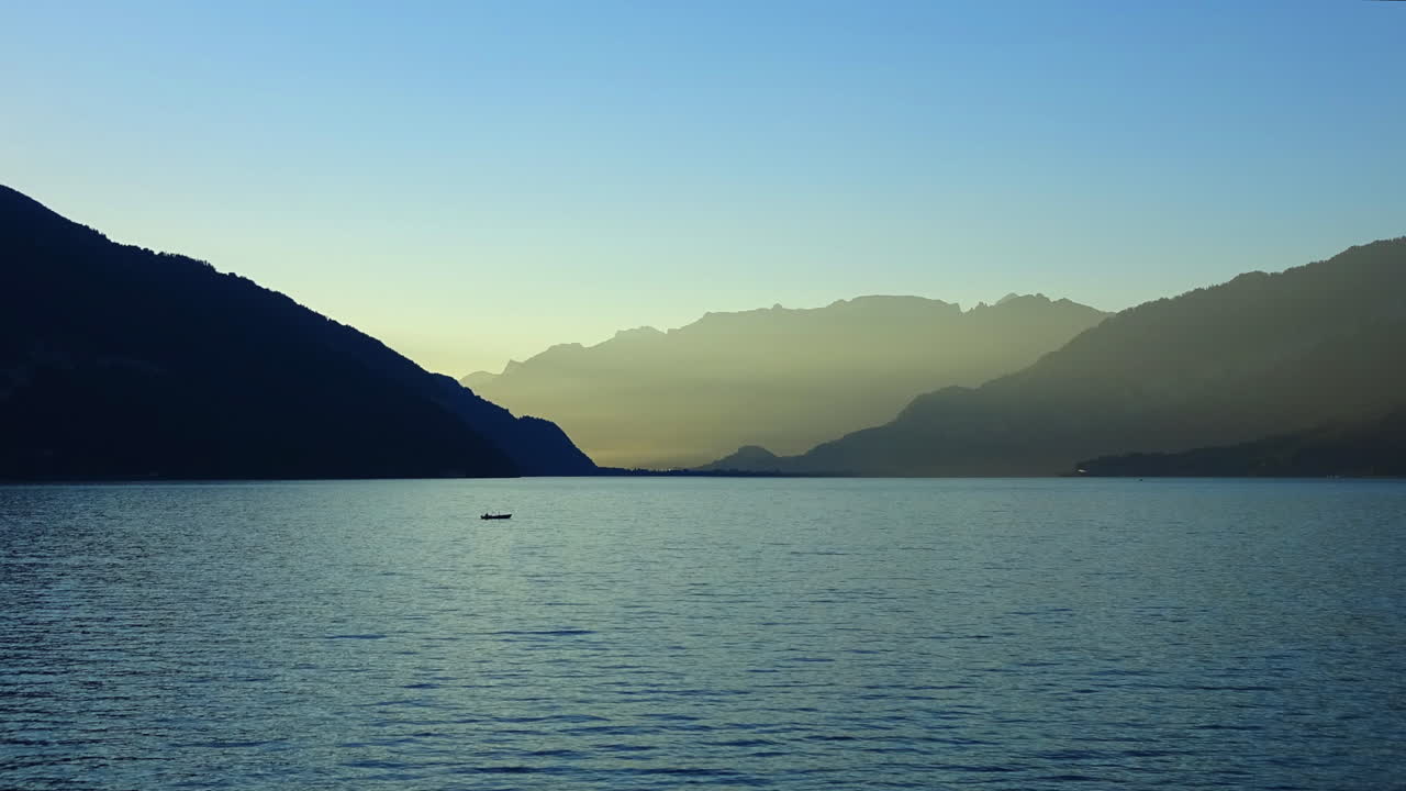 Filmato in timelapse di acqua calma sul Lago di Thun con piccole sagome di barche e montagne alpine stratificate all'ora d'oro a Thun, Berna, Svizzera.
