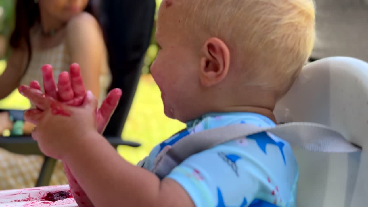Happy baby eating lunch outdoors on summers day and is covered in food