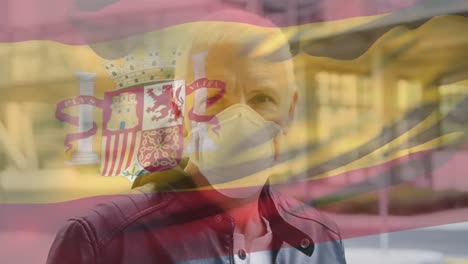 animation of flag of spain waving over man wearing face mask during covid 19 pandemic